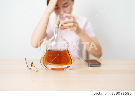 Stressed woman drinking cognac alone with problem. Exhausted drunk man looking stressed and sleepy. Alcohol addiction, Alcoholism, emotional distress and mental health concept 139058589