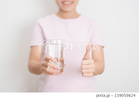 Healthy woman hold glass of clean mineral water and show thumbs up, female drink pure water for hydration and wellness, fresh skin care, daily routine water intake, Refreshment and lifestyle concept Healthy woman hold glass of clean mineral water and show thumbs up, female drink pure water for hydration and wellness, fresh skin care, daily routine water intake, Refreshment and lifestyle concept 139058624