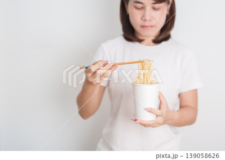 Happy young Asian woman enjoying a delicious cup of hot instant noodles while relaxing at home, Cheerful female eating instant ramen with a smile at apartment. Simple lifestyle and quick meal concept Happy young Asian woman enjoying a delicious cup of hot instant noodles while relaxing at home, Cheerful female eating instant ramen with a smile at apartment. Simple lifestyle and quick meal concept 139058626