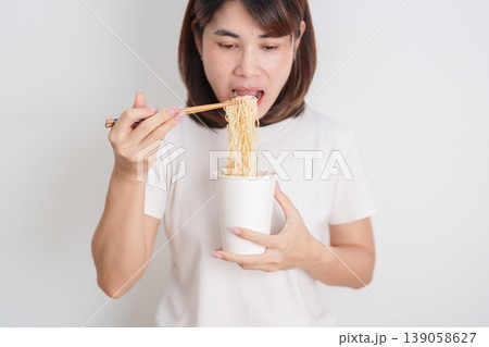 Happy young Asian woman enjoying a delicious cup of hot instant noodles while relaxing at home, Cheerful female eating instant ramen with a smile at apartment. Simple lifestyle and quick meal concept Happy young Asian woman enjoying a delicious cup of hot instant noodles while relaxing at home, Cheerful female eating instant ramen with a smile at apartment. Simple lifestyle and quick meal concept 139058627