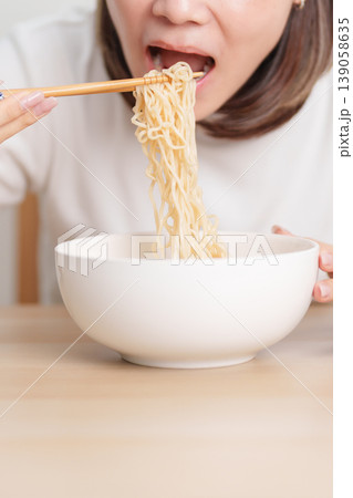 Happy young Asian woman enjoying a delicious bowl of hot instant noodles while relaxing at home, Cheerful female eating instant ramen with a smile at apartment. Simple lifestyle and quick meal concept Happy young Asian woman enjoying a delicious bowl of hot instant noodles while relaxing at home, Cheerful female eating instant ramen with a smile at apartment. Simple lifestyle and quick meal concept 139058635