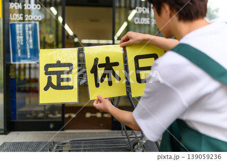 男性店員が定休日のお知らせを貼る 男性店員が定休日のお知らせを貼る 139059236