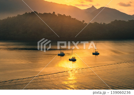 Aerial view of catamaran yachts anchored in a calm tropical bay during golden hour. Aerial view of catamaran yachts anchored in a calm tropical bay during golden hour. 139060236