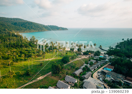 Aerial view of a tropical island resort village nestled between lush forest and the beach. 139060239