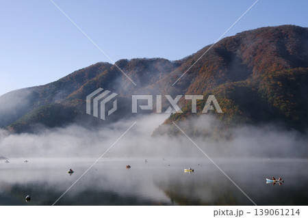 秋、朝霧の立ち込める精進湖。紅葉の山肌と釣りの小舟が幻想的で印象的深い。 139061214