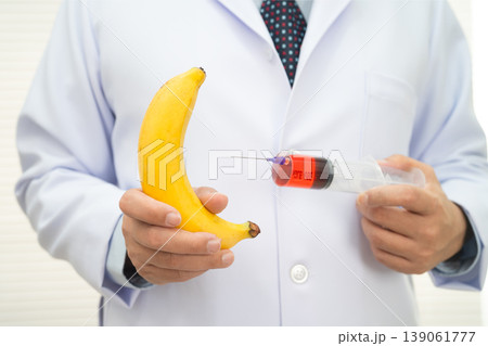 Male doctor making an injection to a banana with a syringe, penis health. Male doctor making an injection to a banana with a syringe, penis health. 139061777