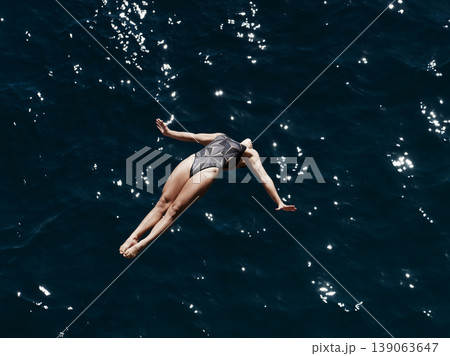 a professional female diver is jumping off a cliff into the sea a professional female diver is jumping off a cliff into the sea 139063647
