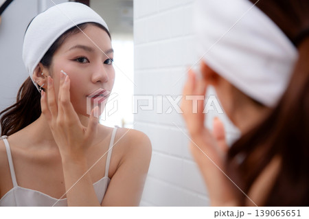 Beautiful asian woman applying cream or lotion for rejuvenation skin on face while looking mirror. Beautiful asian woman applying cream or lotion for rejuvenation skin on face while looking mirror. 139065651