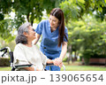 Young caucasian nurse comforting with patient while sitting on wheelchair in outdoor park. 139065654