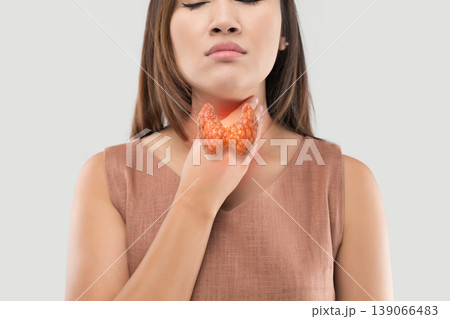 A woman holding her throat, illustrating potential thyroid pathology. 139066483