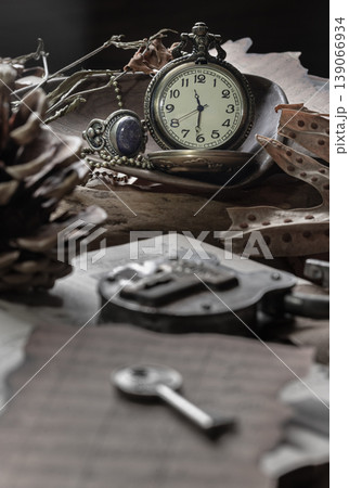 a classic pocket watch perches on weathered wood, its hands frozen against an ivory face. Nearby, a silver filigree ring with a midnight-blue stone glints beside a rustic skeleton key and archaic a classic pocket watch perches on weathered wood, its hands frozen against an ivory face. Nearby, a silver filigree ring with a midnight-blue stone glints beside a rustic skeleton key and archaic 139066934