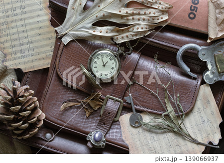 A symphony of sepia and stone, this still life captures a vintage satchel draped in the remnants of a bygone era. An open watch counts the silent seconds among charred musical scores and weathered A symphony of sepia and stone, this still life captures a vintage satchel draped in the remnants of a bygone era. An open watch counts the silent seconds among charred musical scores and weathered 139066937