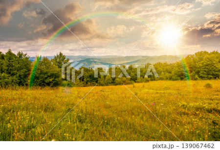 sunset over mountainous rural landscape in summertime. picturesque highland woods and grassy meadow. view of countryside scenery with forested hills behind the pasture under rainbow sunset over mountainous rural landscape in summertime. picturesque highland woods and grassy meadow. view of countryside scenery with forested hills behind the pasture under rainbow 139067462