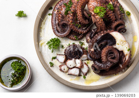 Boiled octopus on ceramic plate with olive oil and parsley dressing top view. Seafood appetizer Boiled octopus on ceramic plate with olive oil and parsley dressing top view. Seafood appetizer 139069203