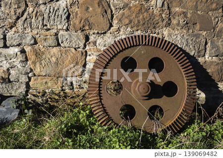 Old rusty gear leaning against stone wall Old rusty gear leaning against stone wall 139069482