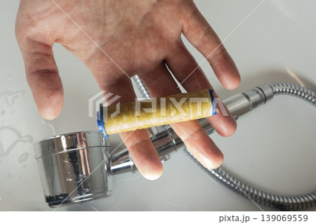 Hand holding old rusty shower filter during water filter replacement process 139069559