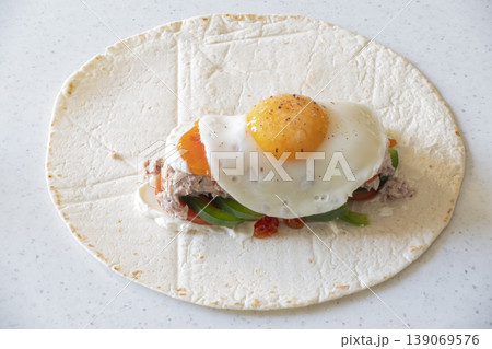 Tortilla wrap with mozzarella, vegetables, tuna, and fried egg on white background Tortilla wrap with mozzarella, vegetables, tuna, and fried egg on white background 139069576