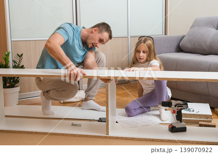father and daughter carefully align furniture pieces together on the floor while surrounded by assembly tools and parts in a bright modern living room 139070922