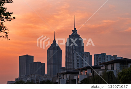 Twin spired skyscrapers and urban residential complexes standing tall against a captivating orange sunset sky Twin spired skyscrapers and urban residential complexes standing tall against a captivating orange sunset sky 139071087