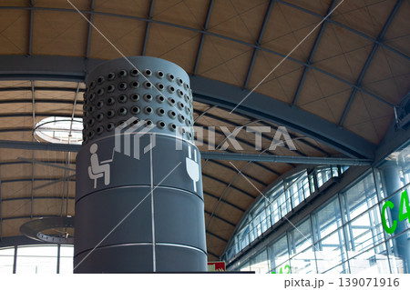 Column with icons indicating seating and charging stations inside a modern airport terminal with a high ceiling and large windows Column with icons indicating seating and charging stations inside a modern airport terminal with a high ceiling and large windows 139071916