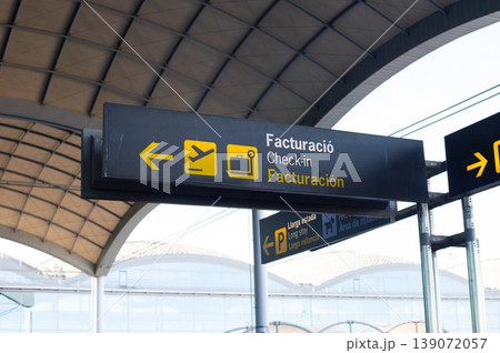 Airport signage indicating check-in direction with icons for flight and luggage under a modern architectural structure 139072057
