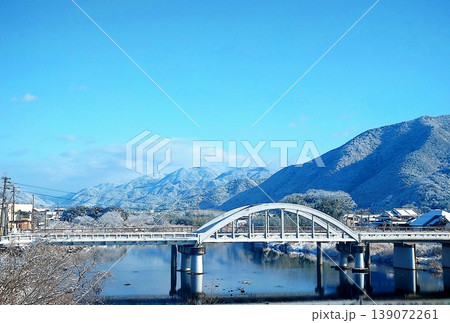 雪化粧の山並みとアーチ橋が架かる冬の川風景　青空に映える静かな日本の景観 139072261
