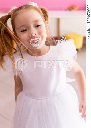 Little birthday girl with cake on face laughing at party Little birthday girl with cake on face laughing at party 139072603