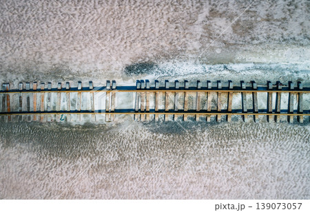 Old railway sleepers and rails cross a vast pink salt flat, showcasing textures and patterns from an aerial view Old railway sleepers and rails cross a vast pink salt flat, showcasing textures and patterns from an aerial view 139073057