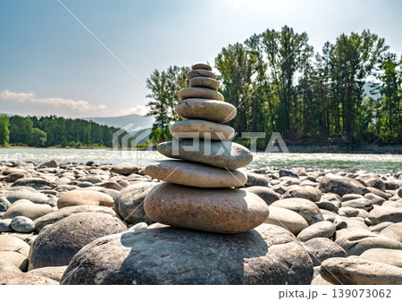 Smooth river stones creating a balanced cairn on a sunny riverbank, with a flowing river and green forest Smooth river stones creating a balanced cairn on a sunny riverbank, with a flowing river and green forest 139073062