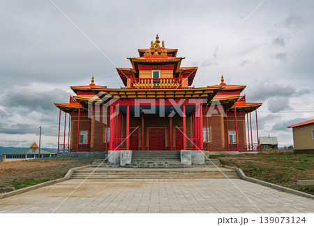 Majestic Datsan architecture with tiered roofs and vibrant colors under a cloudy sky in a remote steppe landscape Majestic Datsan architecture with tiered roofs and vibrant colors under a cloudy sky in a remote steppe landscape 139073124