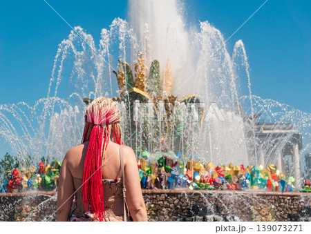Woman with bright red and blonde braids observes the grand Friendship of Peoples Fountain at VDNKh in Moscow Woman with bright red and blonde braids observes the grand Friendship of Peoples Fountain at VDNKh in Moscow 139073271