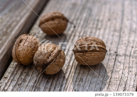 Closeup of four whole walnuts on aged wooden surface with natural textures and warm tones. Organic food, natural patterns, textures, and healthy nutrition. Copy space. Selective focus 139073379
