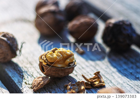 Closeup of cracked open walnut with exposed kernel on rustic wood, surrounded by whole nuts and shells. Fresh walnut half with visible nutmeat on textured wooden surface. Selective focus Closeup of cracked open walnut with exposed kernel on rustic wood, surrounded by whole nuts and shells. Fresh walnut half with visible nutmeat on textured wooden surface. Selective focus 139073383
