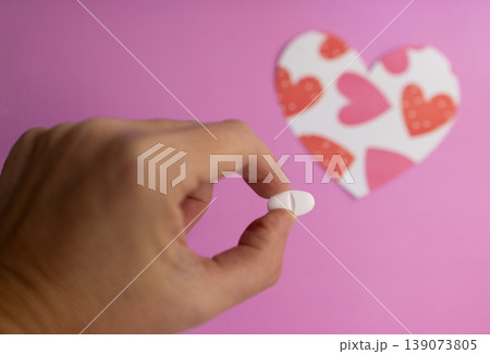Close-up of fingers holding a pill. Background with blurred heart figure 139073805