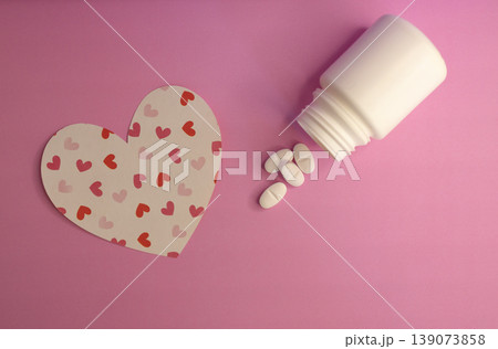 Heart-shaped figure with white capsule bottle on pink background. Heart-shaped figure with white capsule bottle on pink background. 139073858