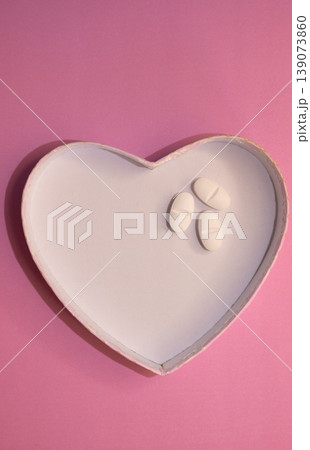 Vertical shot of heart-shaped figure with pills on pink background. 139073860
