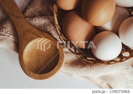 Farm fresh eggs in a rustic woven basket with a natural wooden spoon on a beige textile.Healthy nutrition and baking ingredients Farm fresh eggs in a rustic woven basket with a natural wooden spoon on a beige textile.Healthy nutrition and baking ingredients 139073968