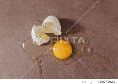 Cracked egg yolk and albumen spilling on a dark counter, symbolizing fresh nutrition, protein source and healthy diet 139073983