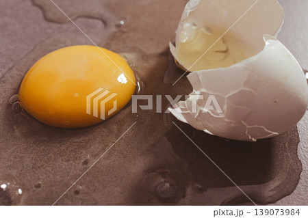 Cracked egg releasing its vibrant yolk and clear albumen onto a textured surface symbolizing fresh nutrition and healthy diet 139073984