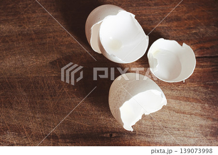 Top view of cracked white eggshells on a rustic wooden surface, showing the empty interior.Sustainable kitchen waste concept 139073998