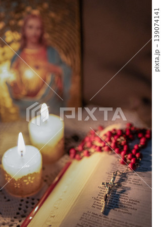 Red rosary on The Bible, illuminated by candlelight.Blurred background. 139074141