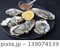 Khasan oysters, live, fresh, opened. Served with classic French Mignonette sauce and half a lemon. Blue plate, black background. Selective focus, close-up. 139074539