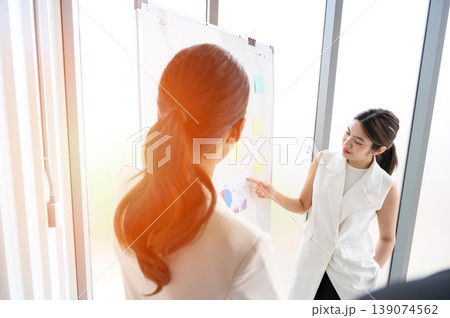 Businesswoman pointing towards graph and giving presentation explaining the idea to her business colleagues in the office. Group of Asian businesspeople brainstorms and work as team. Businesswoman pointing towards graph and giving presentation explaining the idea to her business colleagues in the office. Group of Asian businesspeople brainstorms and work as team. 139074562