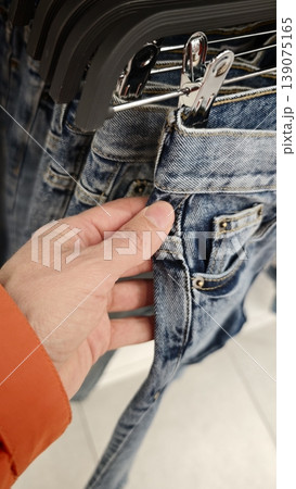 Person holding a pair of jeans while shopping in a clothing store 139075165