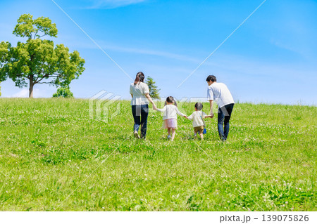 青空の草原を手を繫いで歩く家族 139075826