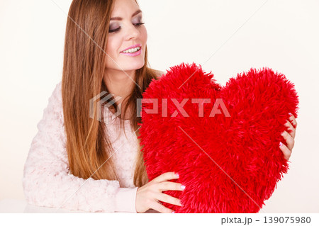 Happy woman holding heart shaped pillow 139075980