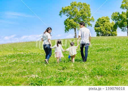 青空の草原を手を繫いで歩く家族 139076018