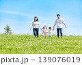 青空の草原を手を繫いで歩く家族 139076019