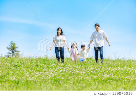 青空の草原を手を繫いで歩く家族 139076019