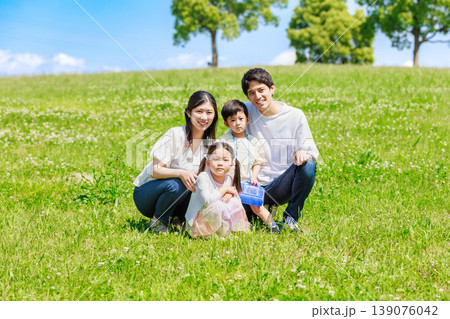 青空の草原に座る家族 139076042